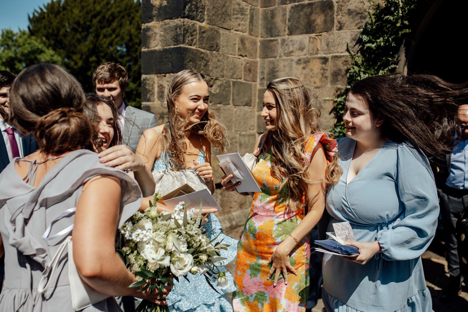 Wedding party in light blue dresses celebrating joyfully outside a stone church building.