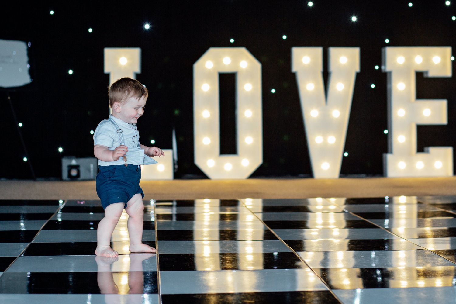 Small child standing on dance floor in front of illuminated LOVE sign.