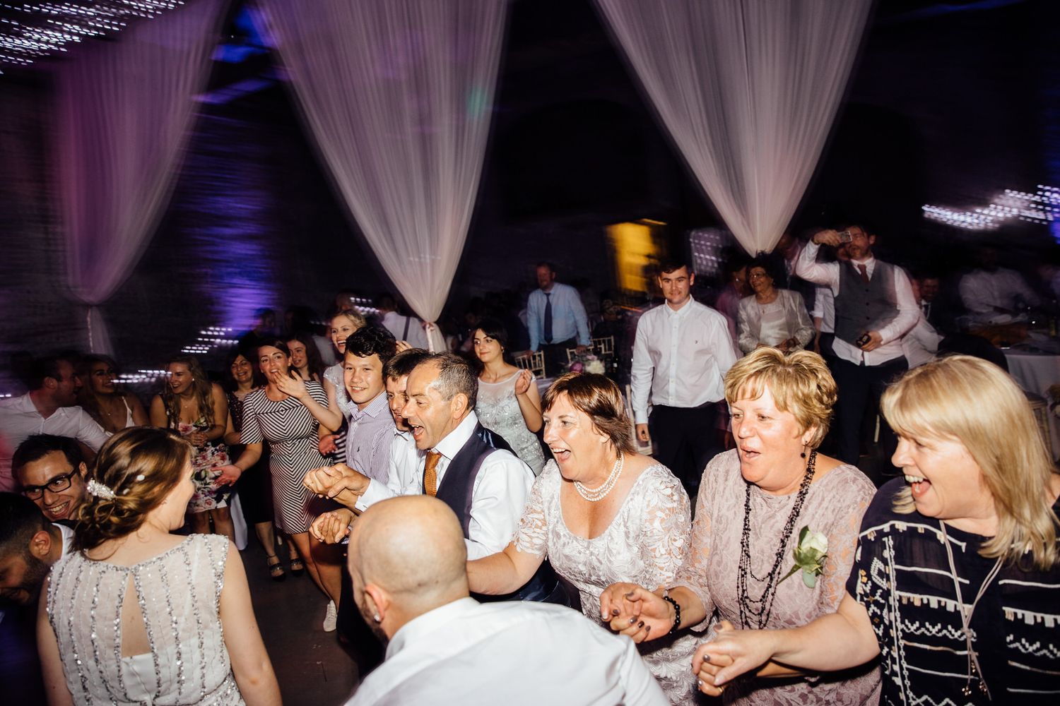Wedding reception dance floor filled with guests under dramatic purple lighting.