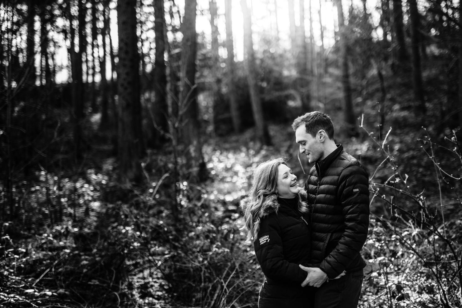 Black and white forest engagement photo session showing couple walking among tall trees.