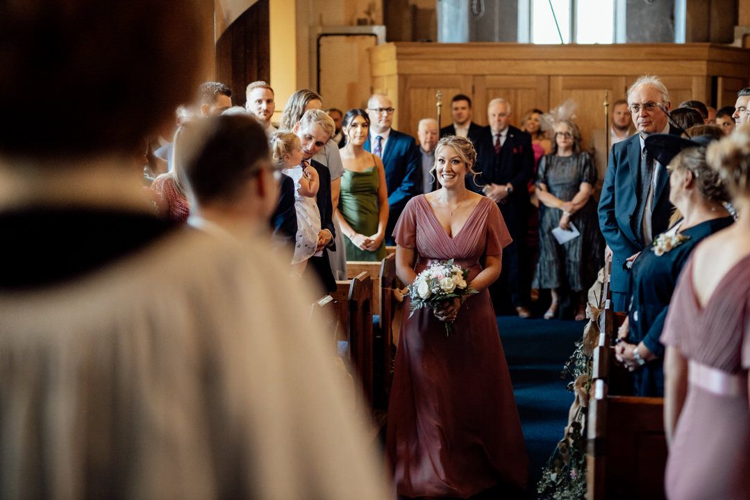 Wedding ceremony guests fill wooden church pews in traditional sanctuary setting.