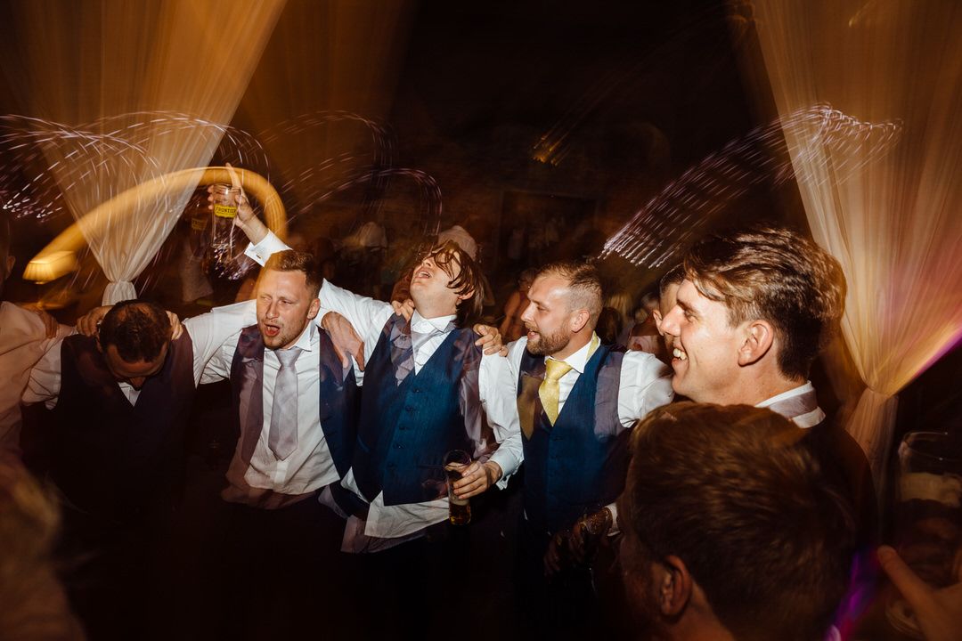 Wedding reception party guests dancing and celebrating in a dimly lit venue.