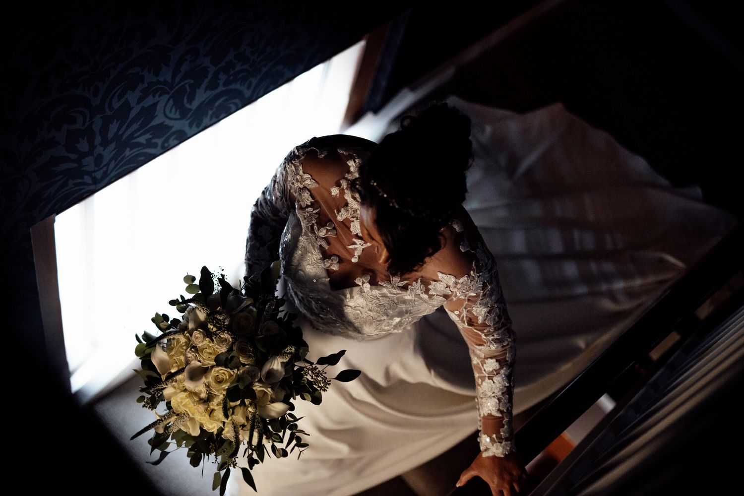Dramatic overhead shot of a bride in lace gown with bouquet against white backdrop.