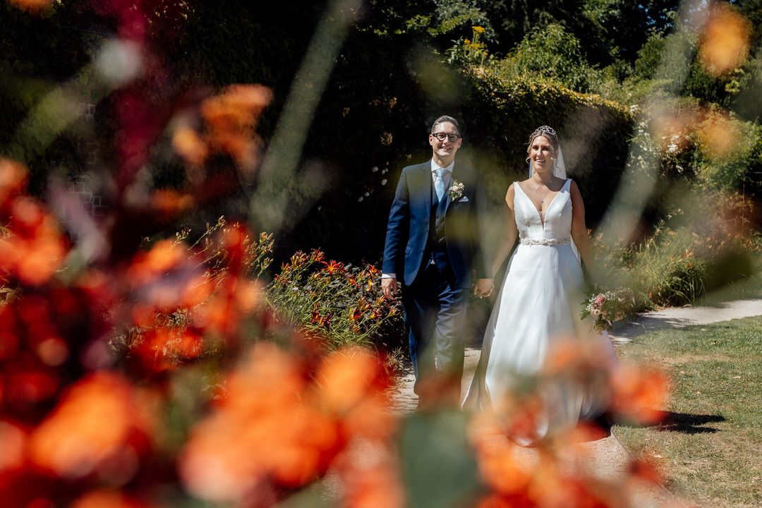 Wedding scene framed through vibrant orange flowers in outdoor garden setting.