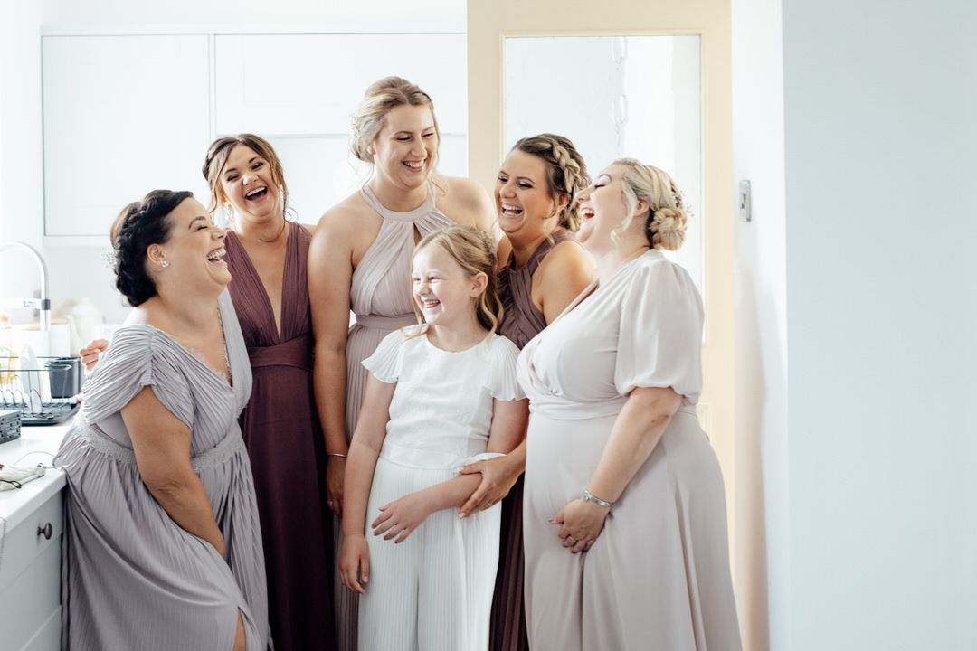 Wedding party members share an emotional moment together in a bright sunlit room.