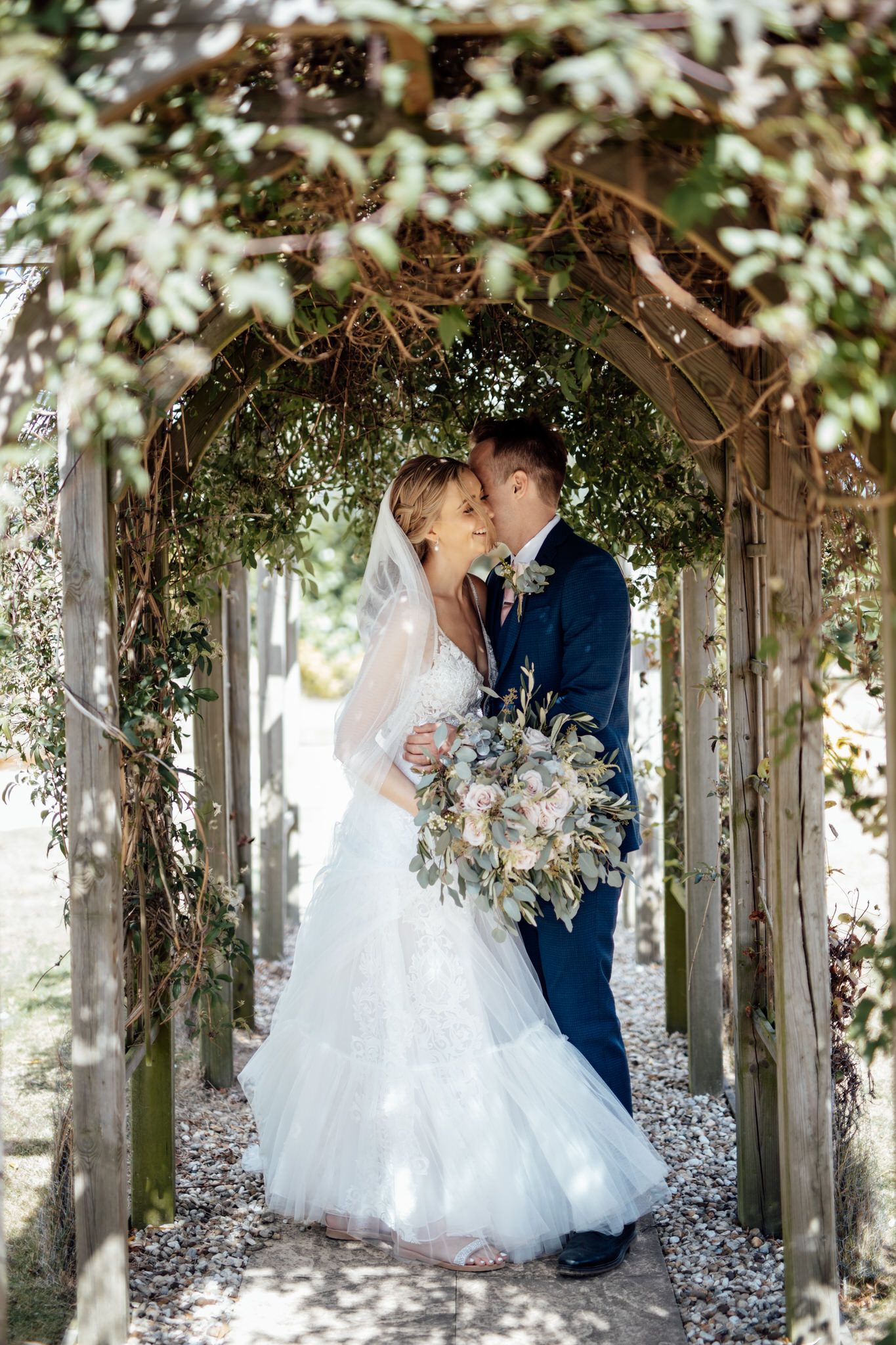 Wedding couple shares intimate moment under floral archway in garden setting.
