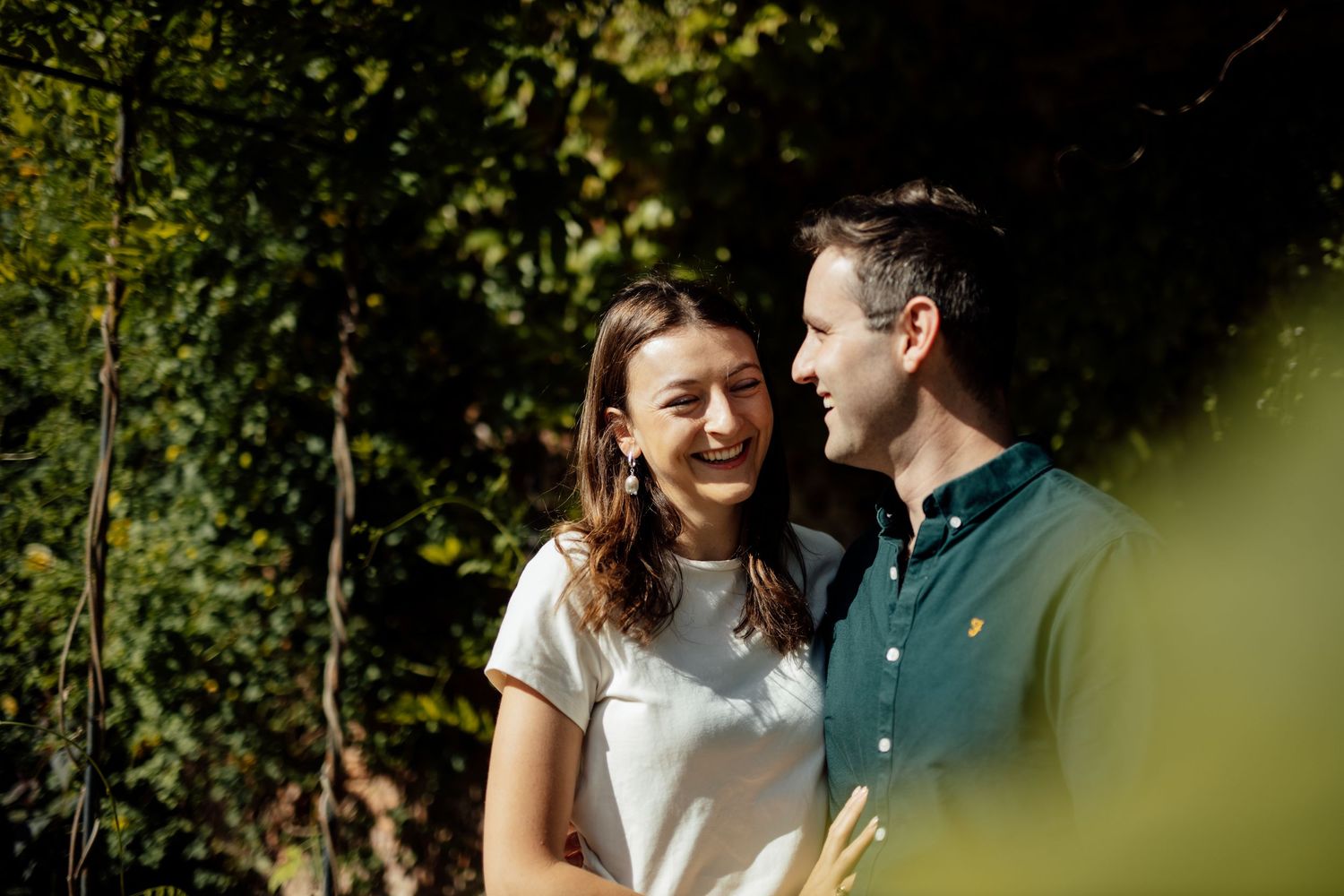 A couple shares joyful moments together in a lush garden setting with natural greenery.