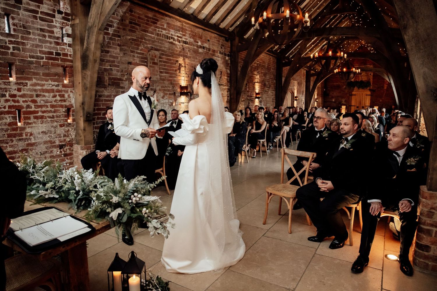 Wedding ceremony taking place in an industrial-style venue with exposed brick walls and chandeliers.
