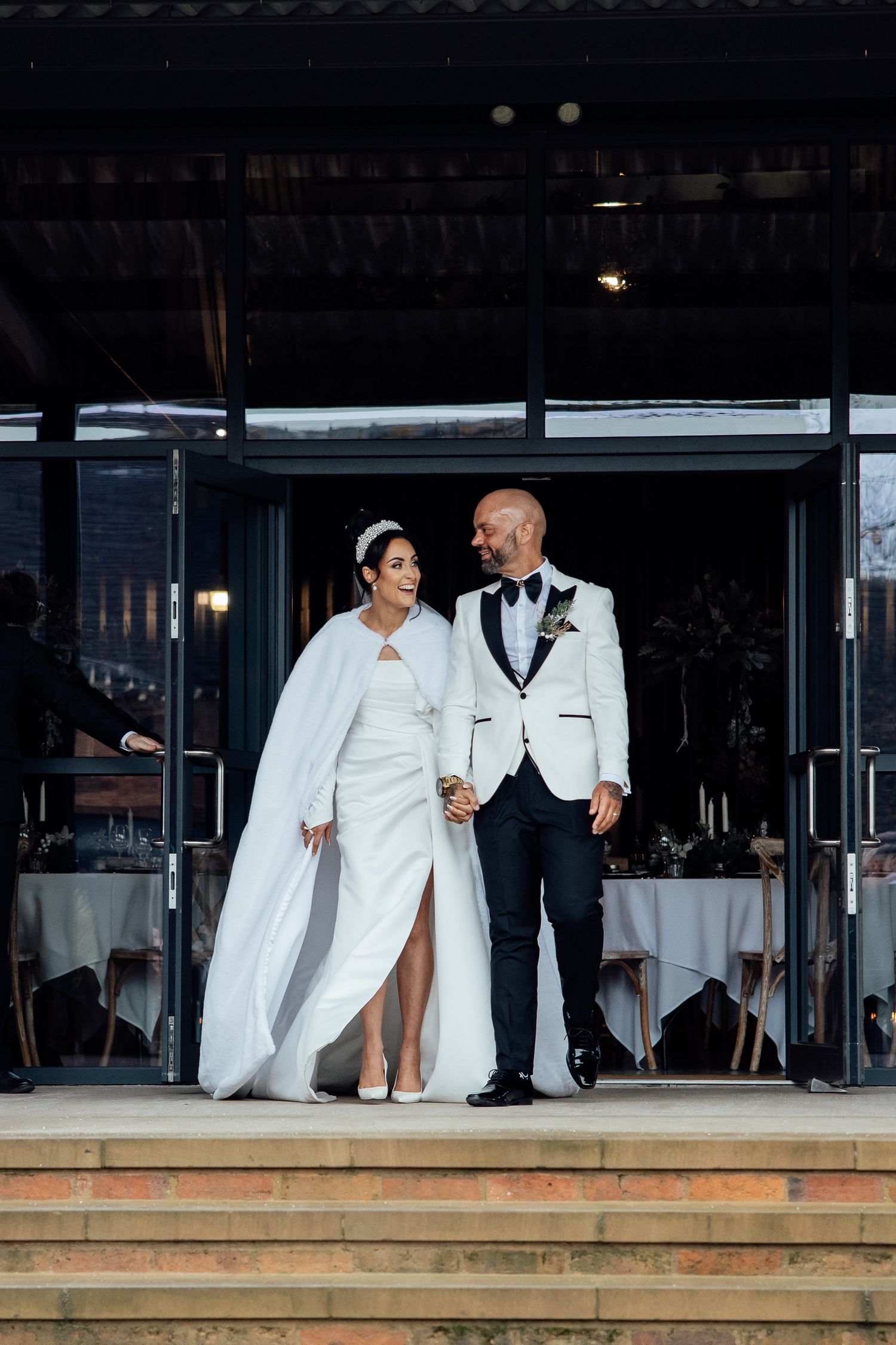 Wedding party members in white attire stand on a wooden deck at an outdoor venue during a celebration.