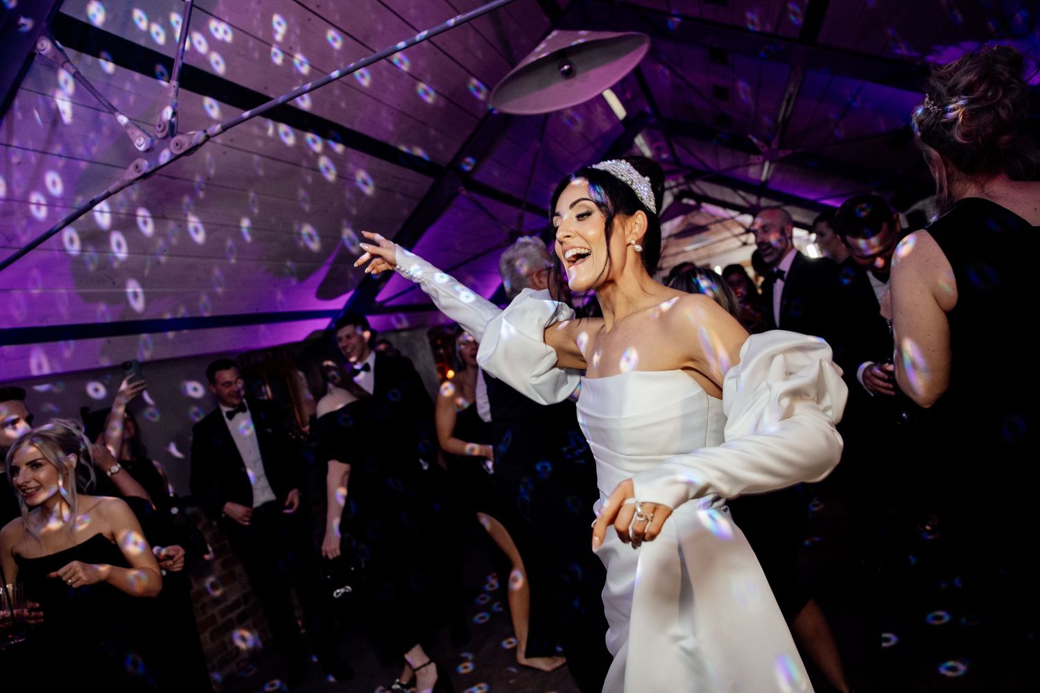 Couples dancing under purple lighting with bubbles floating through the air at an elegant wedding reception.