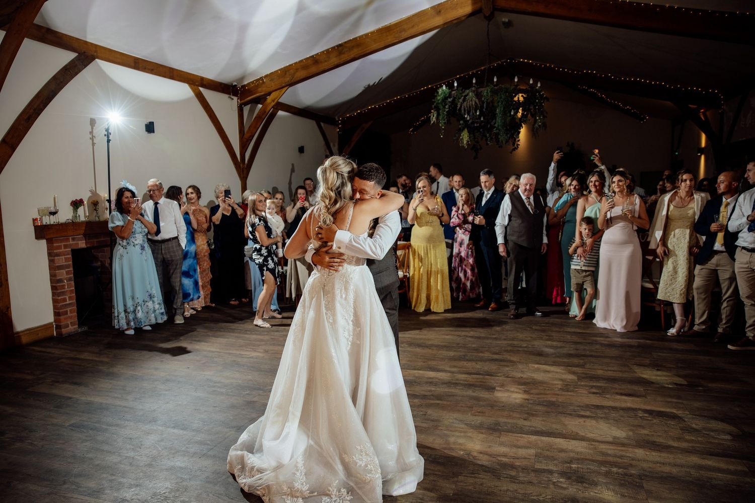 Bride and groom sharing first dance in rustic barn venue surrounded by cheering wedding guests.