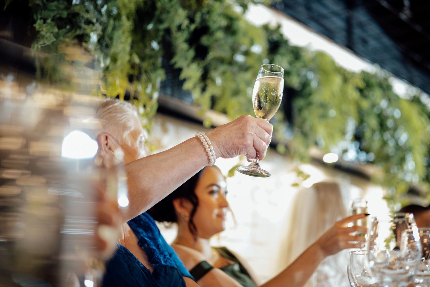An elderly woman raises a champagne glass during a heartfelt wedding toast at the reception.