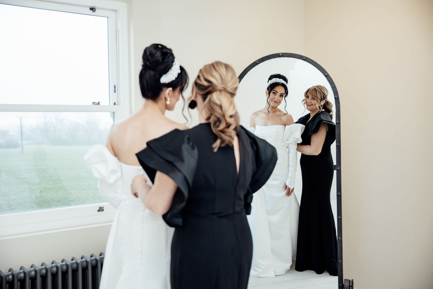 Wedding preparation scene with elegant white dress reflected in a full-length mirror.