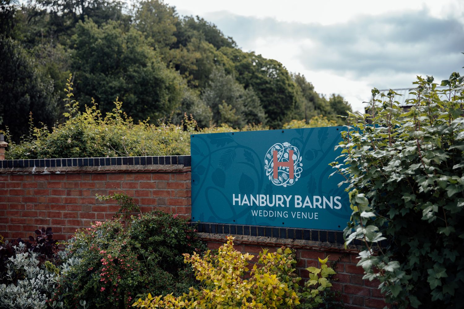 Exterior signage and entrance of Hanbury Barns wedding venue surrounded by greenery.