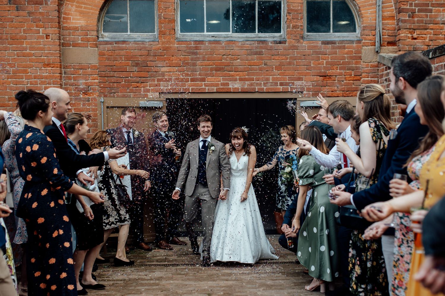 Wedding couple walking through confetti shower with guests lining brick entrance.