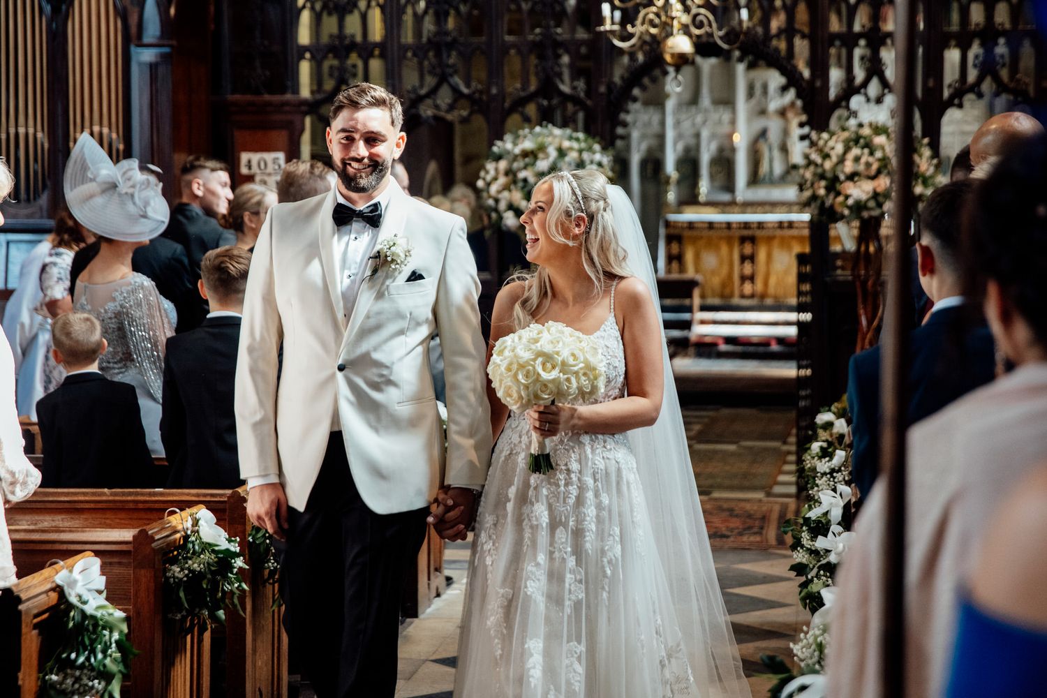 Elegant church wedding ceremony with white floral decorations and guests seated in wooden pews.