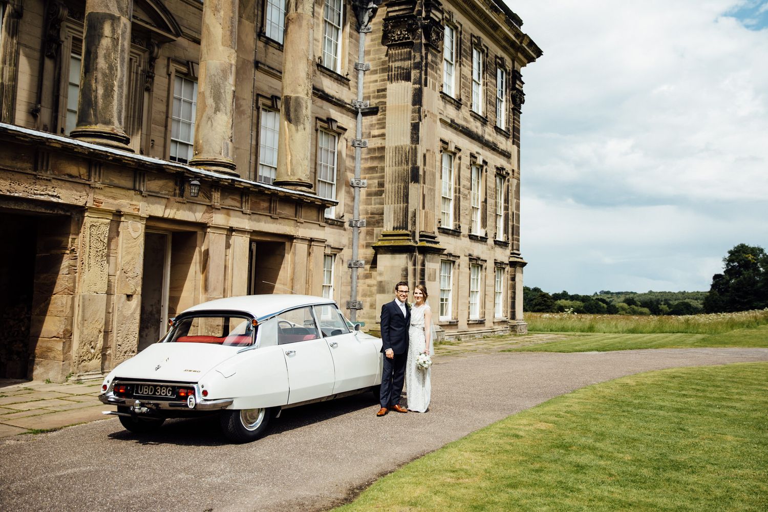Vintage cars parked outside a grand stone mansion with manicured lawns.