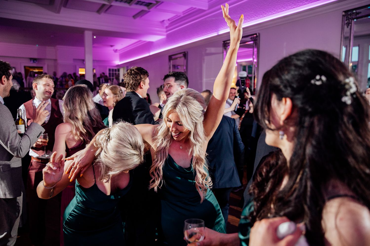 Wedding reception guests dancing enthusiastically under purple mood lighting at a lively party celebration.