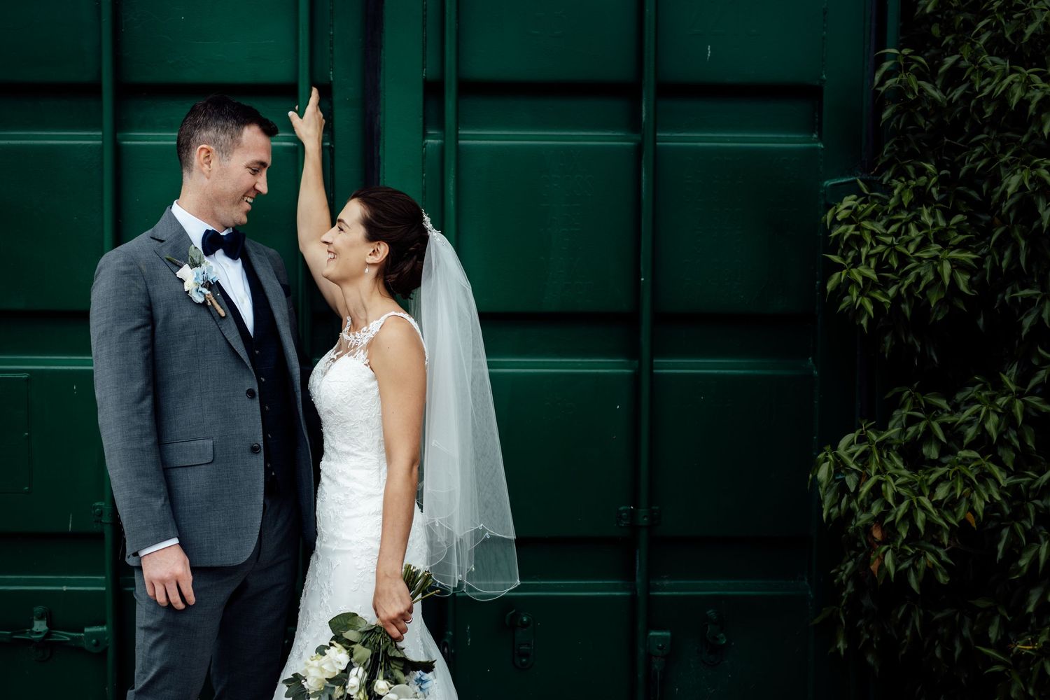 Elegant wedding portrait against a dark green architectural backdrop.
