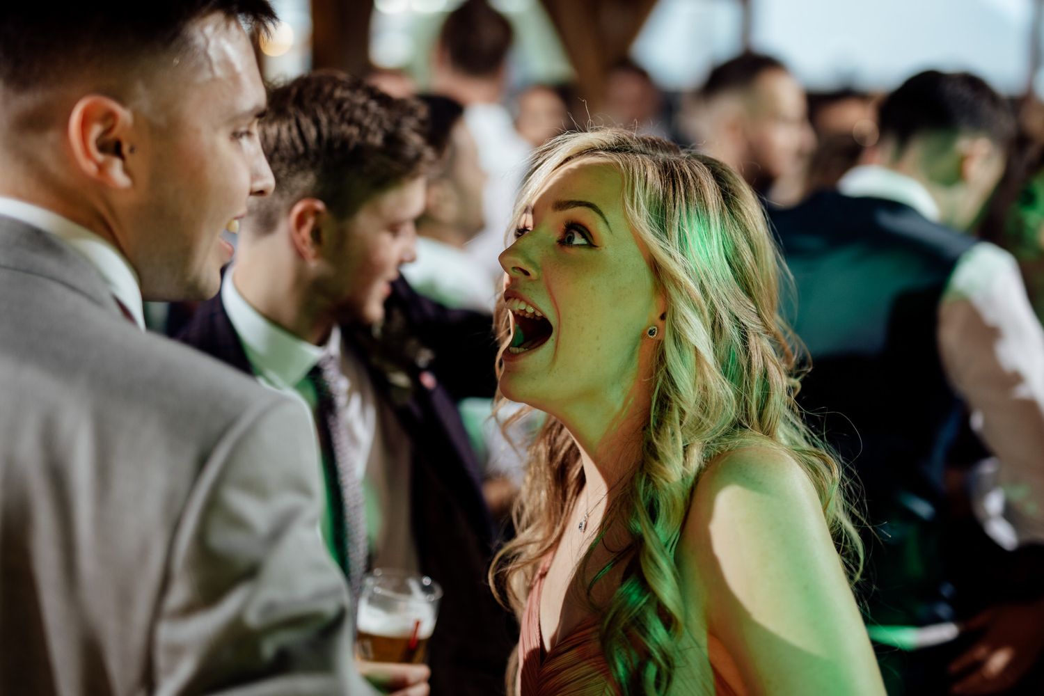 Wedding party dancing and celebrating under atmospheric green lighting.