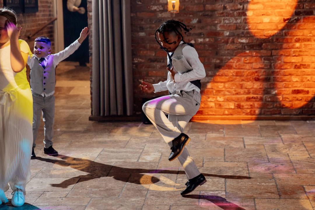 Wedding guests dancing energetically on a stone floor with brick walls and warm lighting.