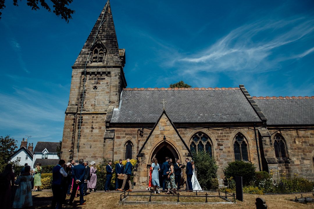 Stone church exterior with Gothic architecture against a bright blue sky on a sunny wedding day.