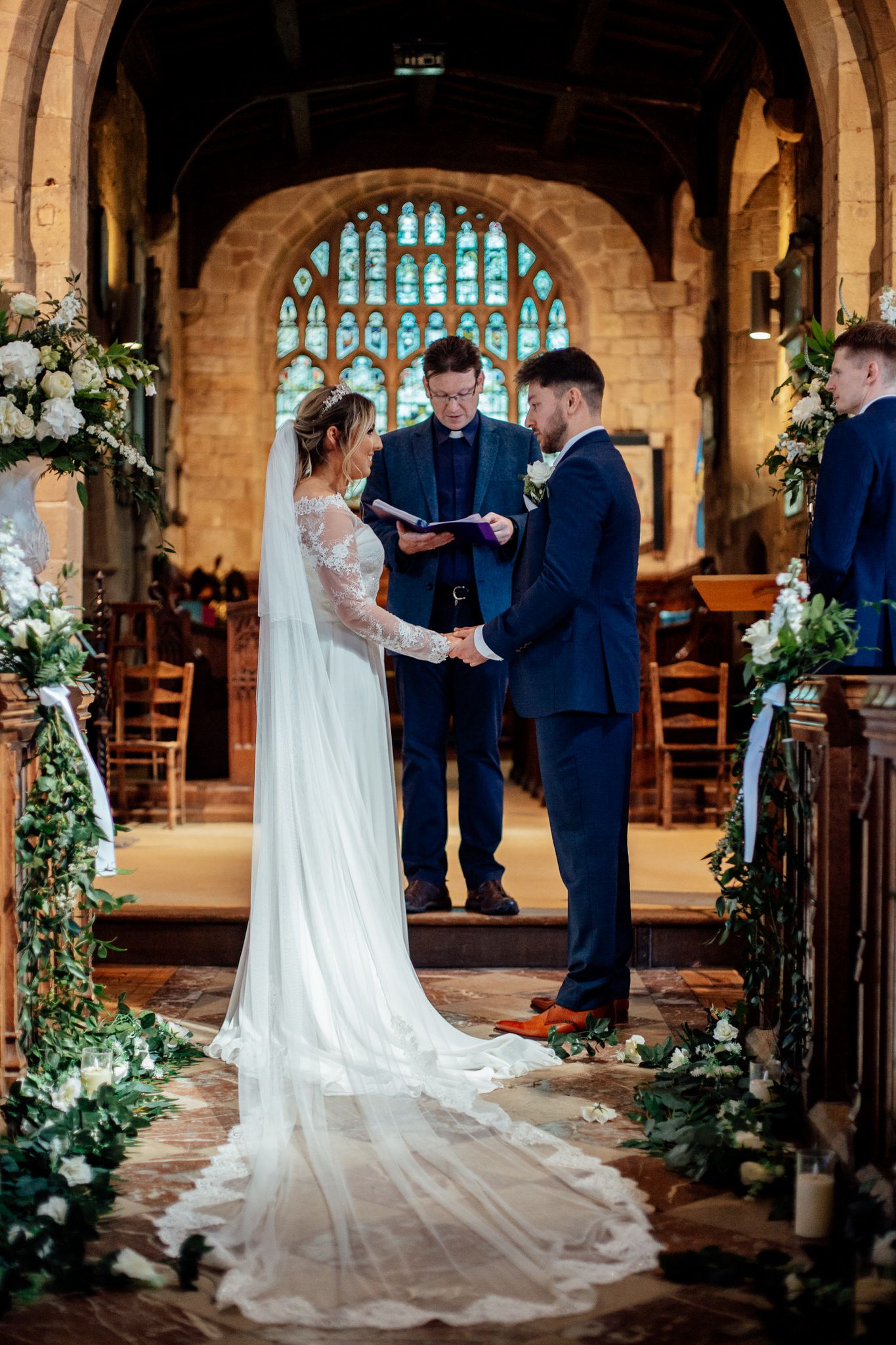 Wedding ceremony in historic church with stone arches and greenery decorations.
