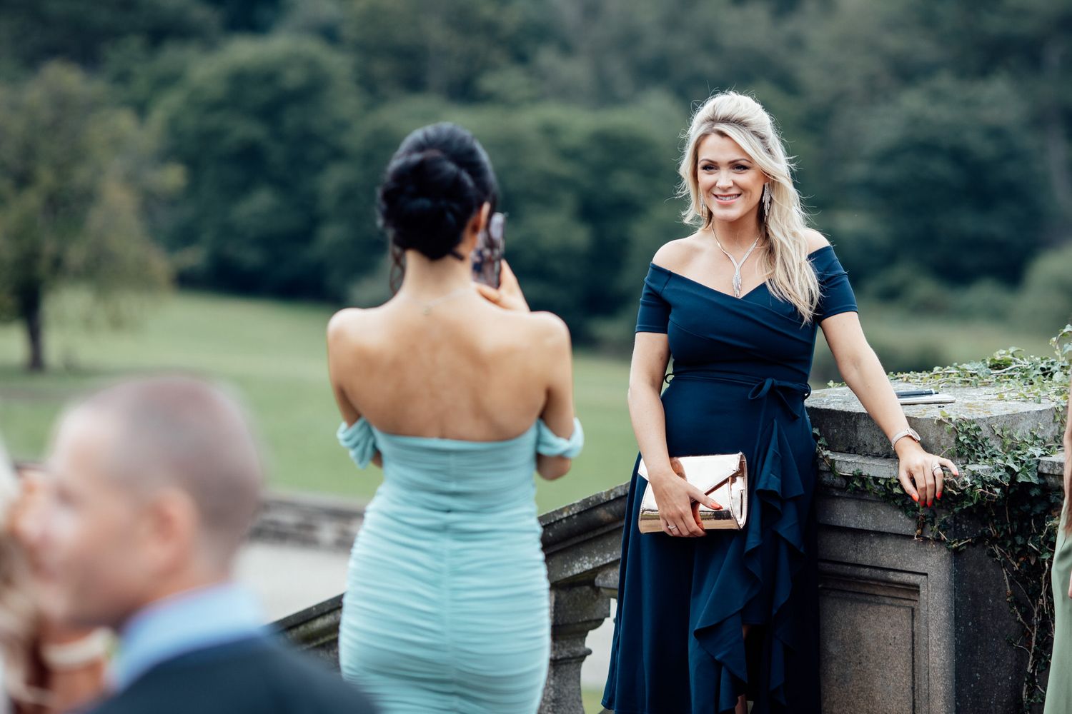Wedding party members in formal attire gather outdoors near stone wall.