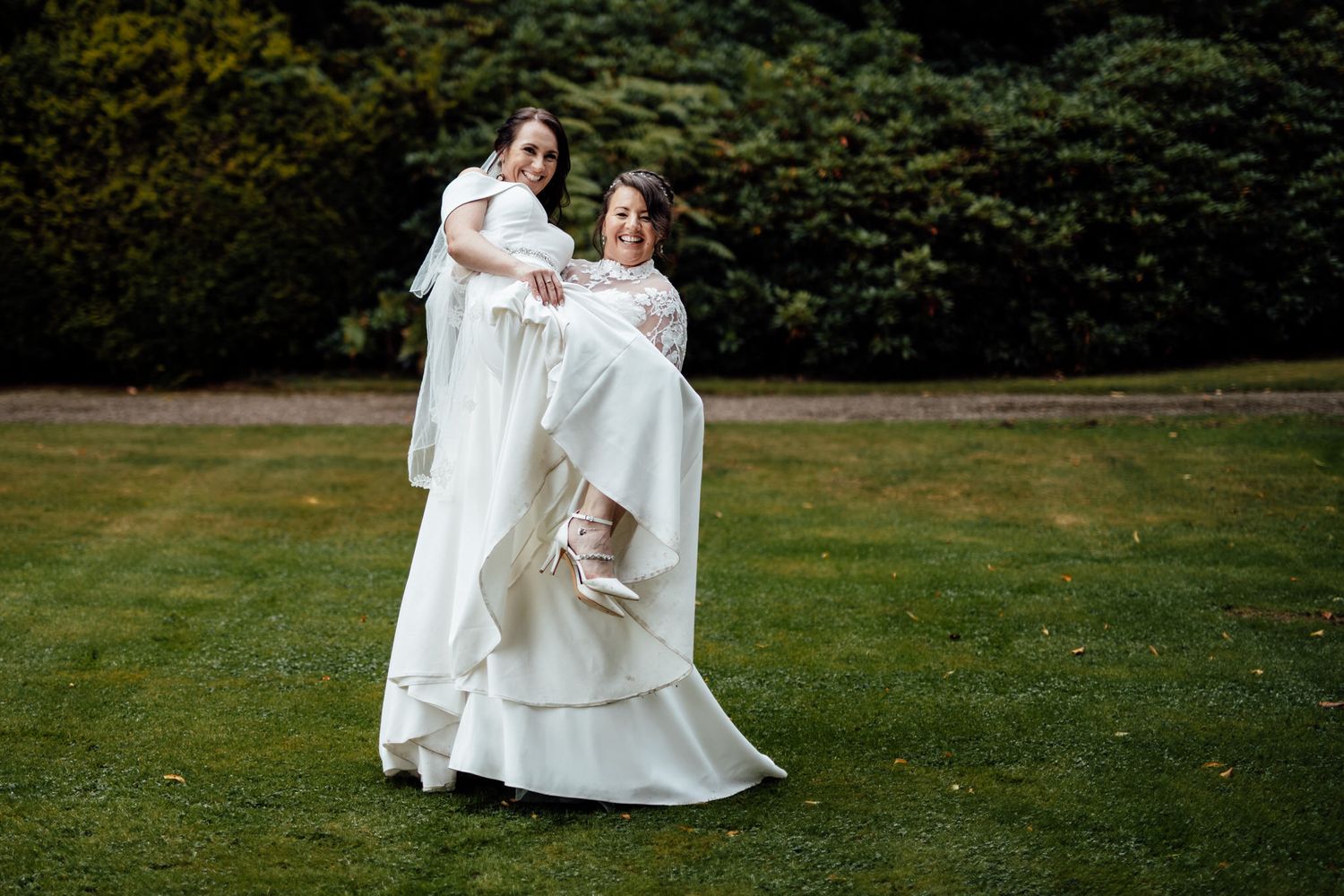 Wedding couple in white dresses walking together on lush green lawn.