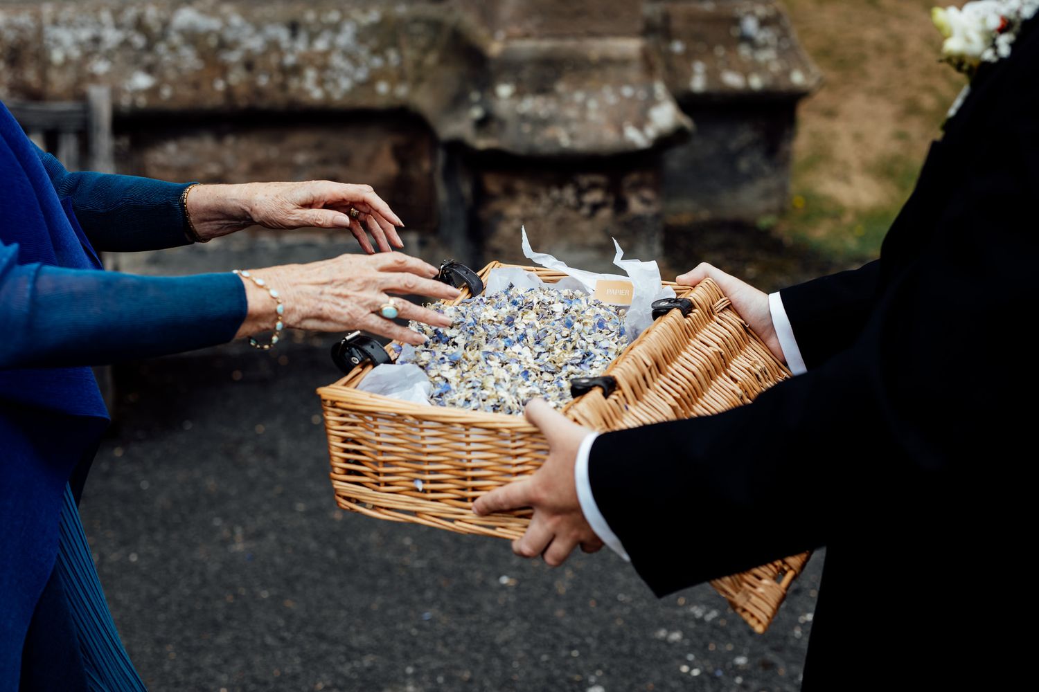 Close-up of hands exchanging wicker baskets at an outdoor wedding event.