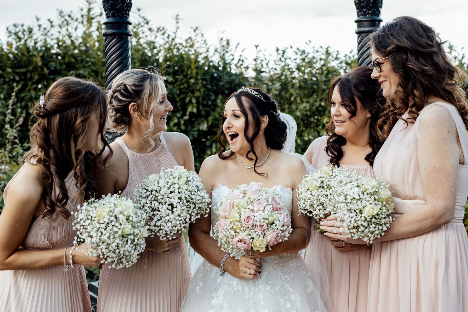 Bridesmaids in blush pink dresses holding baby's breath bouquets in an outdoor garden setting.