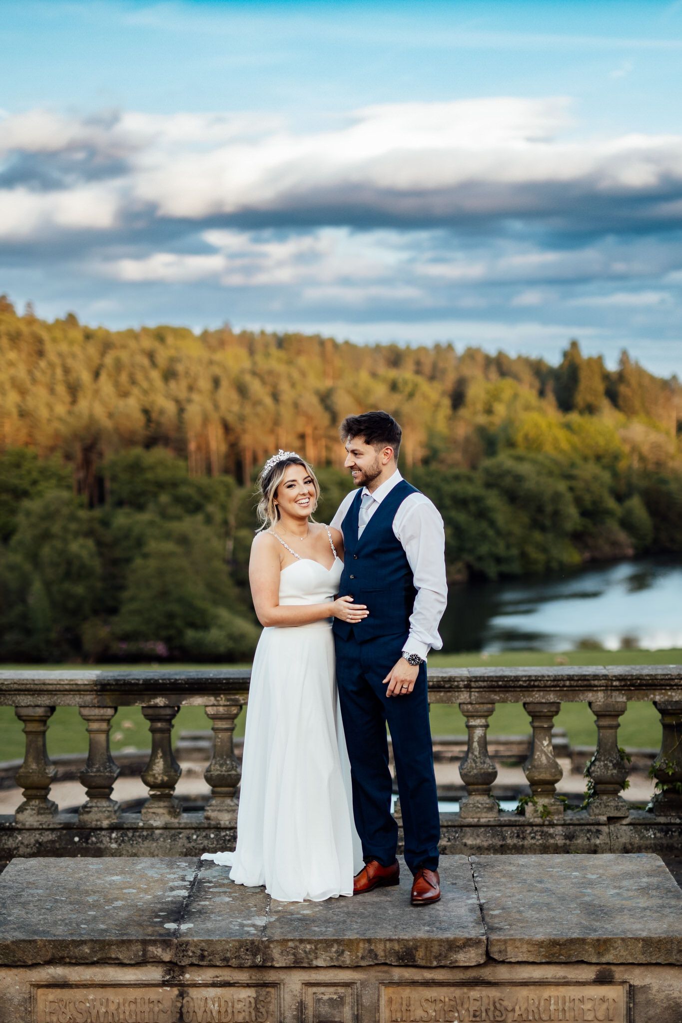Couple standing on stone balcony overlooking scenic river and forest landscape.