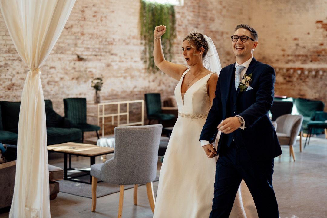 A couple dances together in an elegant brick-walled reception venue with flowing white curtains.