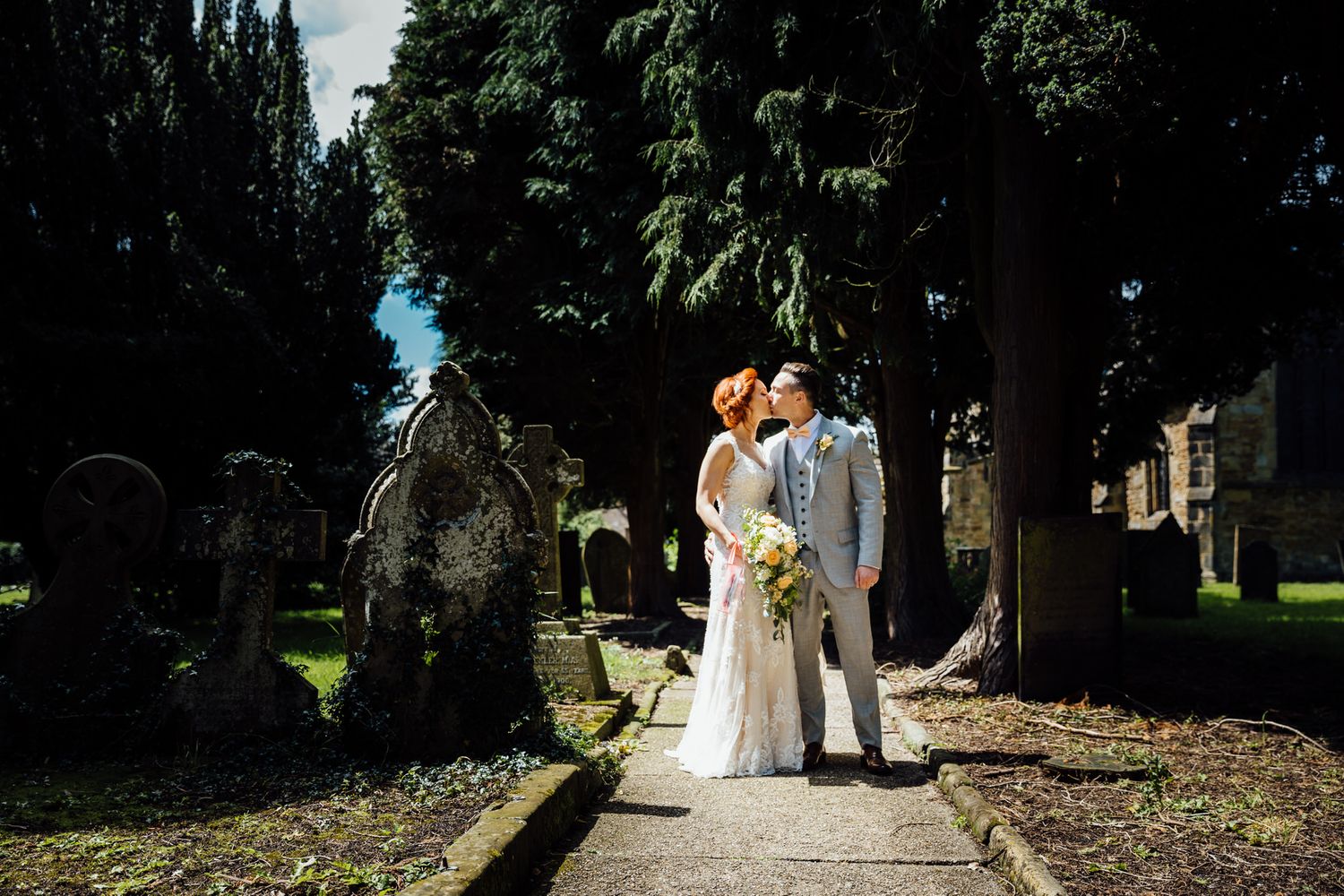 Wedding party poses for outdoor photos on a lush green lawn surrounded by trees.