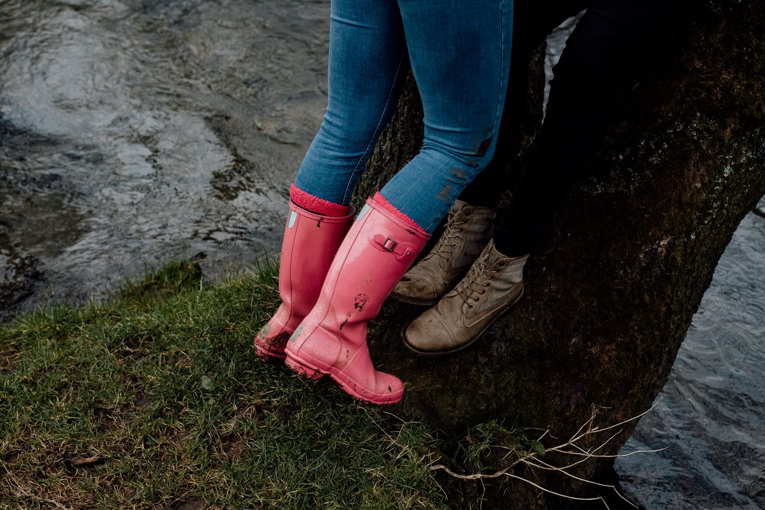 Pink rain boots stand out against dark rocks and flowing water in a romantic outdoor setting.