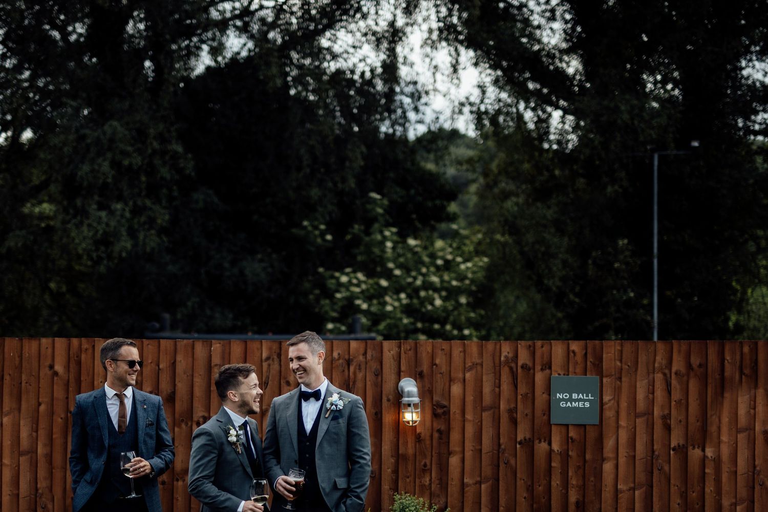 Wedding party poses for photos against a rustic wooden fence backdrop.