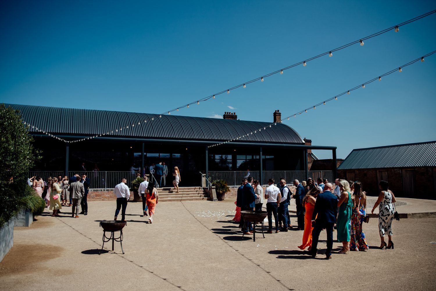 Panoramic view of an outdoor venue with guests gathering under blue summer skies.