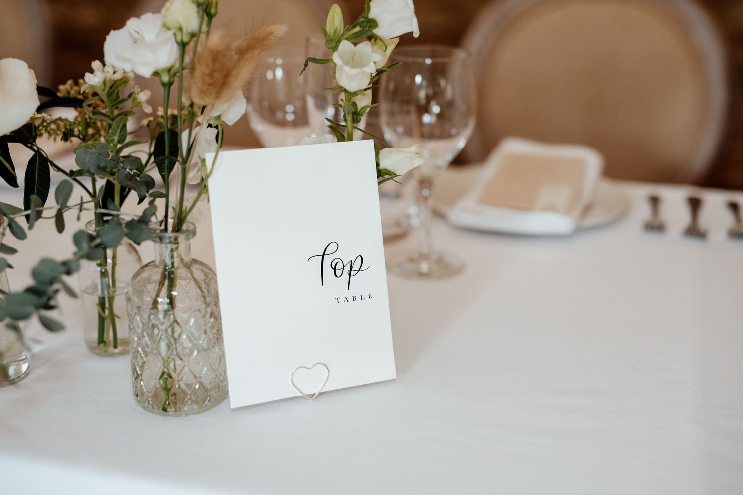 Elegant wedding reception table settings with white floral centerpieces and place cards.
