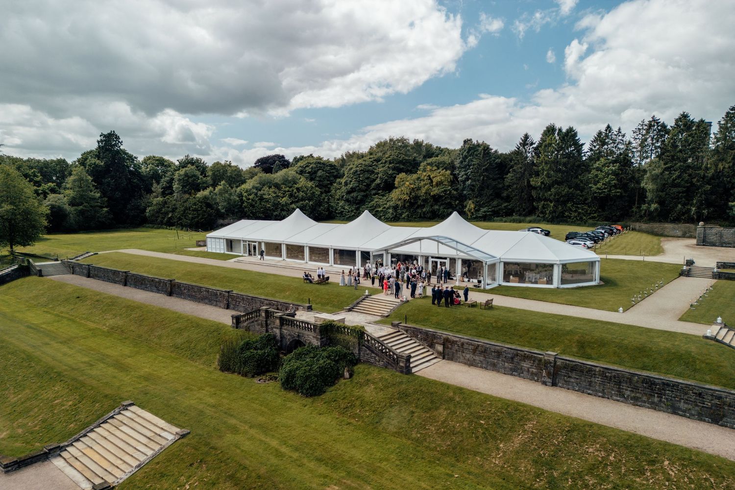 Panoramic drone shot of an elegant white wedding venue nestled in rolling green hills.