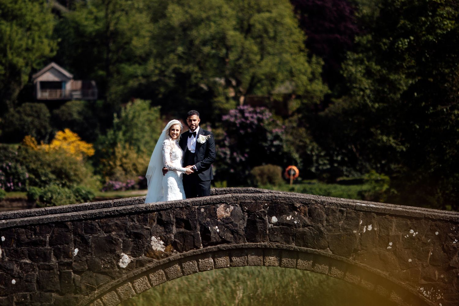 Stone bridge in garden setting creates romantic backdrop for wedding photography.