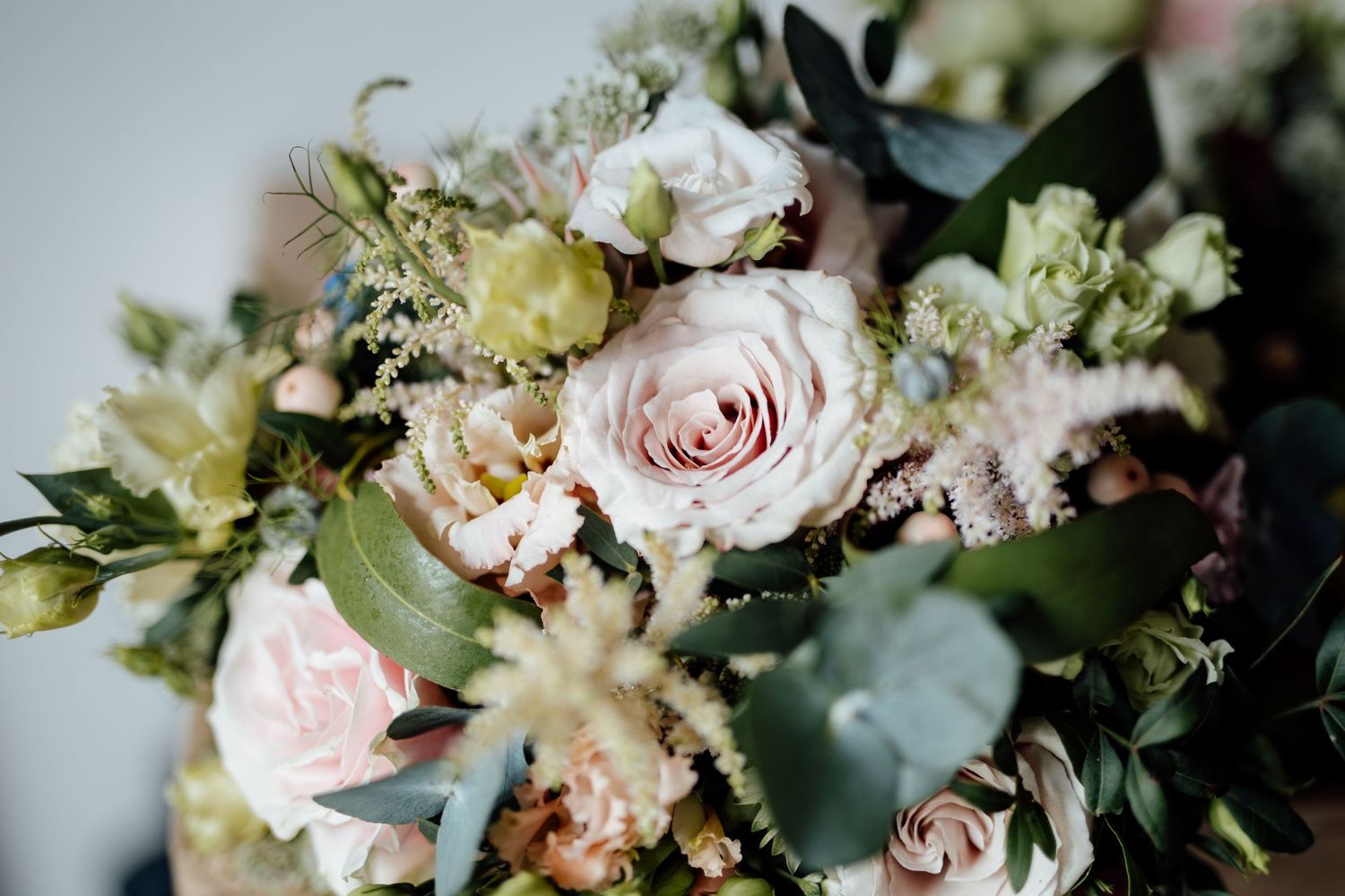Close-up of romantic pastel wedding bouquet with roses and greenery.