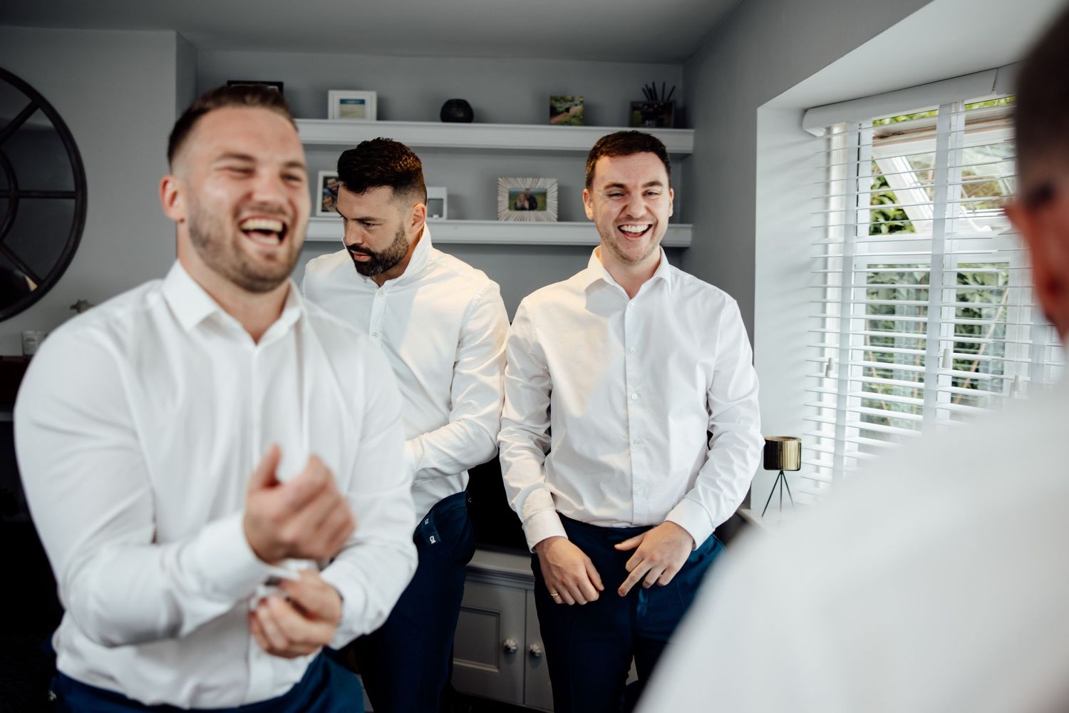 Groomsmen share laughter and smiles while getting ready in formal attire before a wedding celebration.