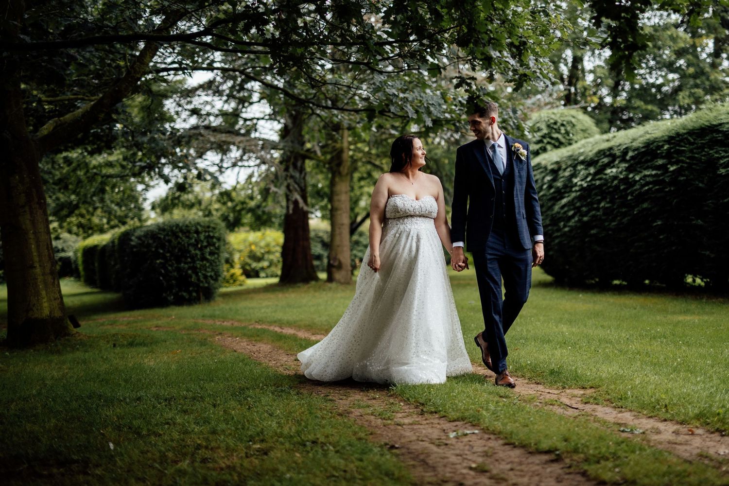 A romantic garden wedding portrait on a tree-lined path.