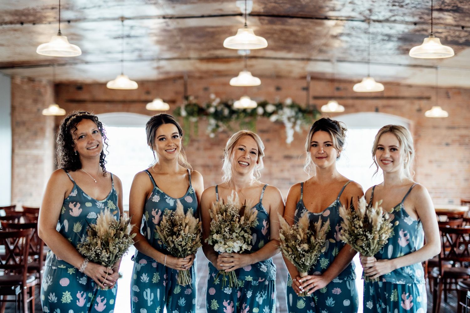Bridesmaids wearing matching floral dresses lined up in an industrial-style venue.