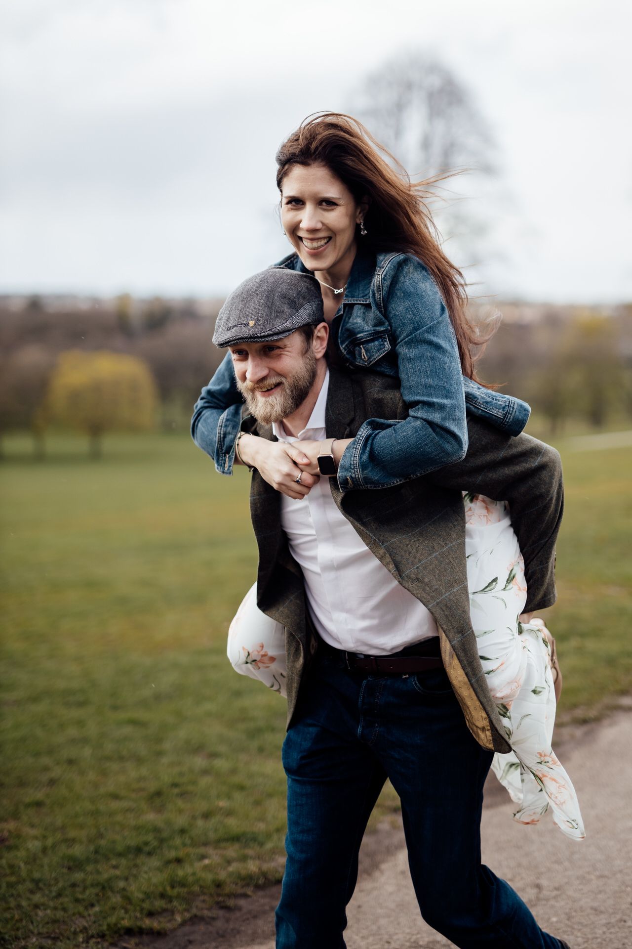 Playful couple having fun with piggyback rides in an open field on a cloudy day.