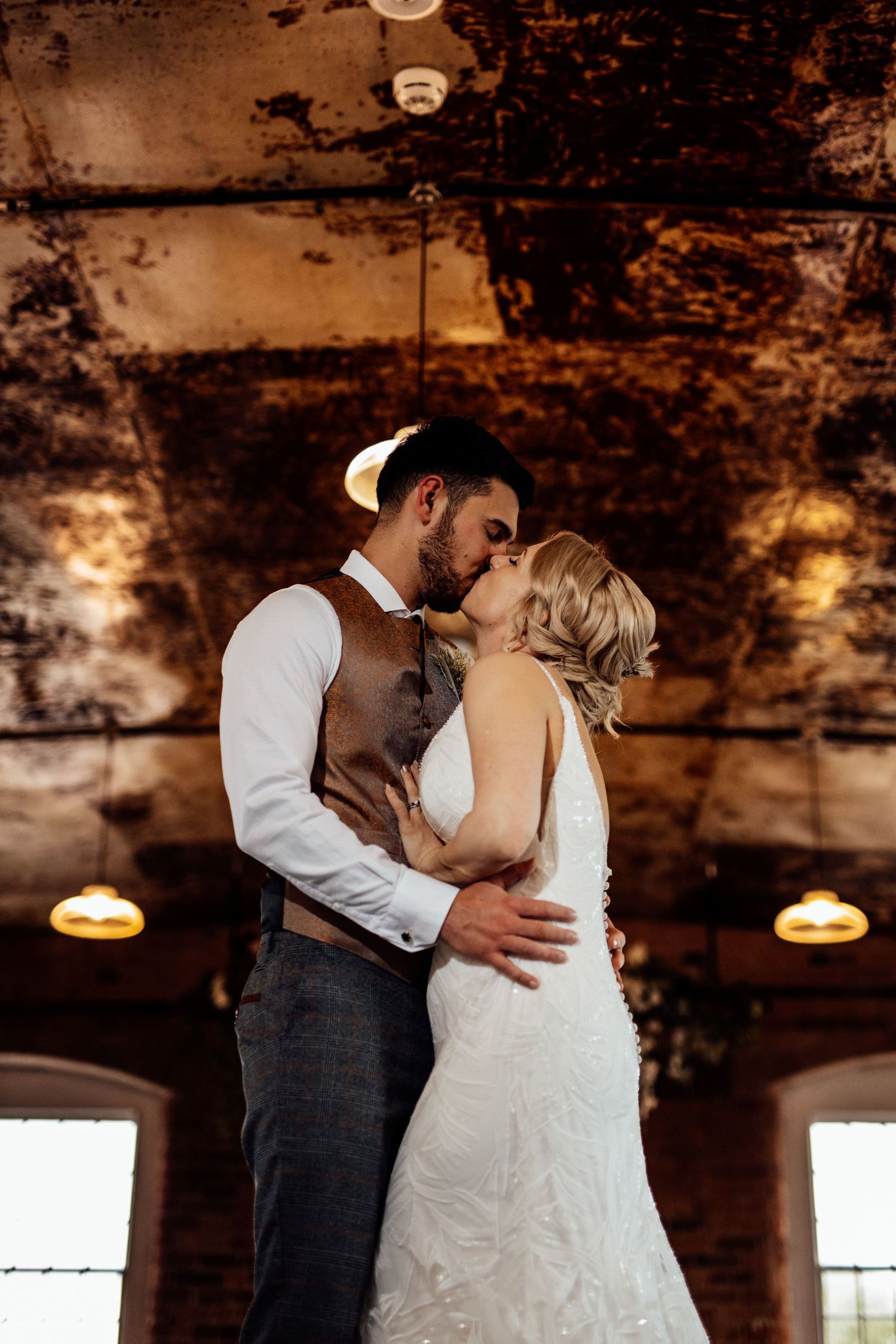 Romantic first dance between newlyweds in rustic venue with exposed brick walls and warm lighting.