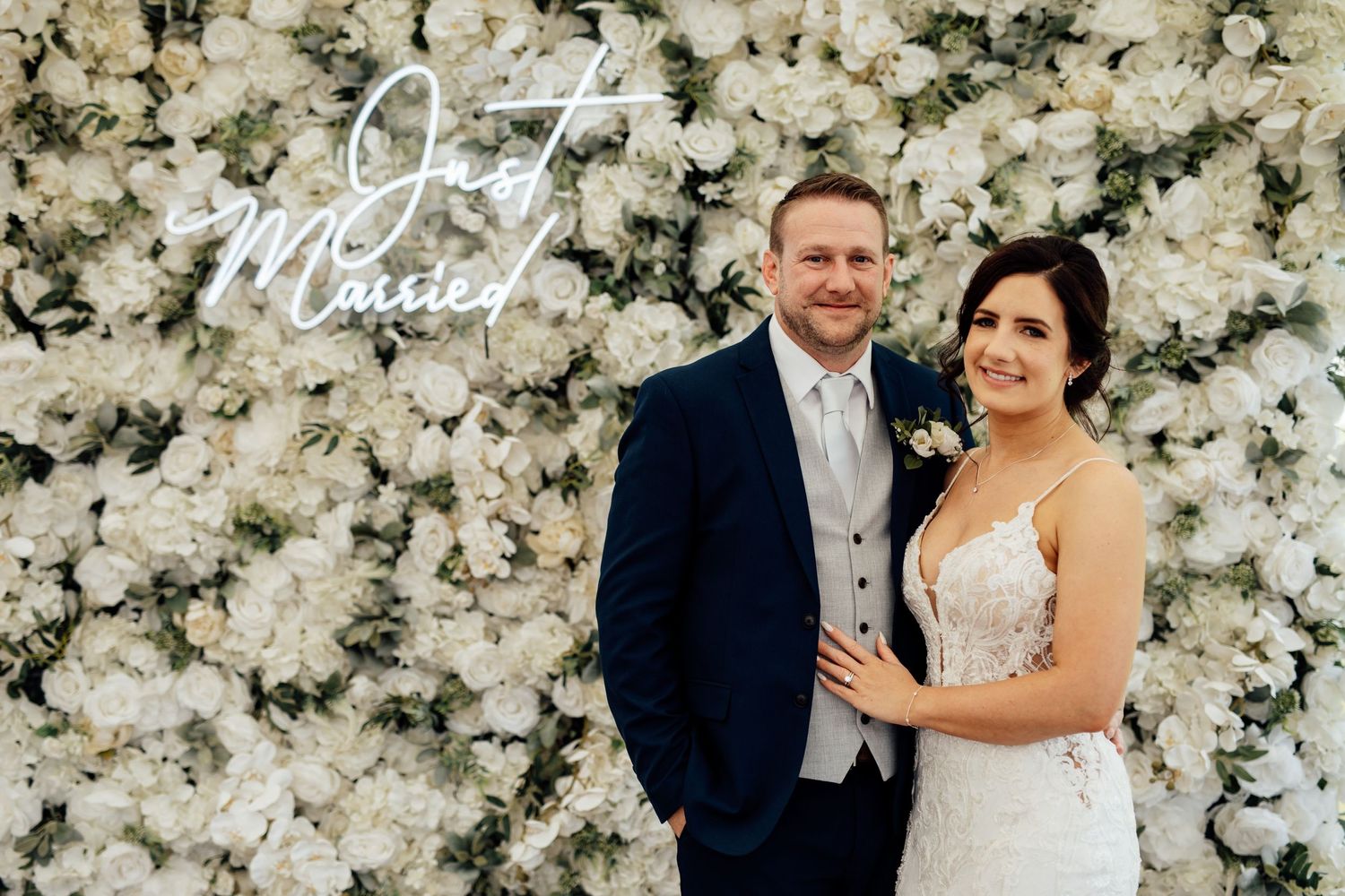 Elegant wedding backdrop featuring a wall of white roses and floral arrangements.