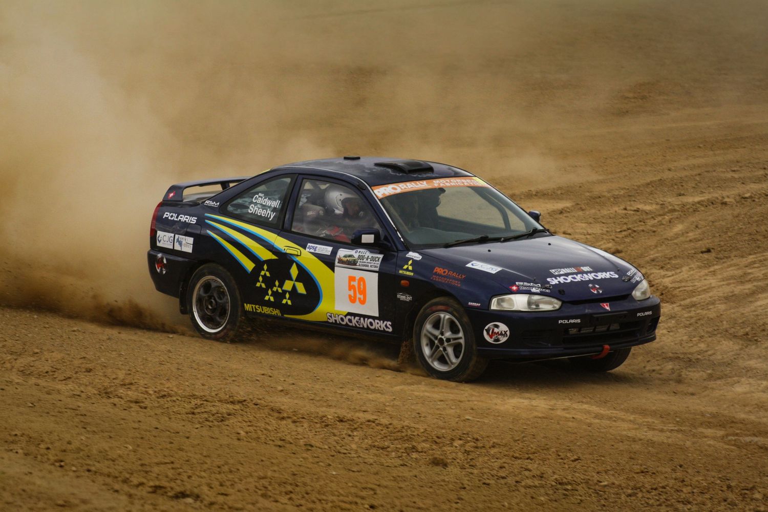 Black Subaru rally car drifting through dirt corner during competition.