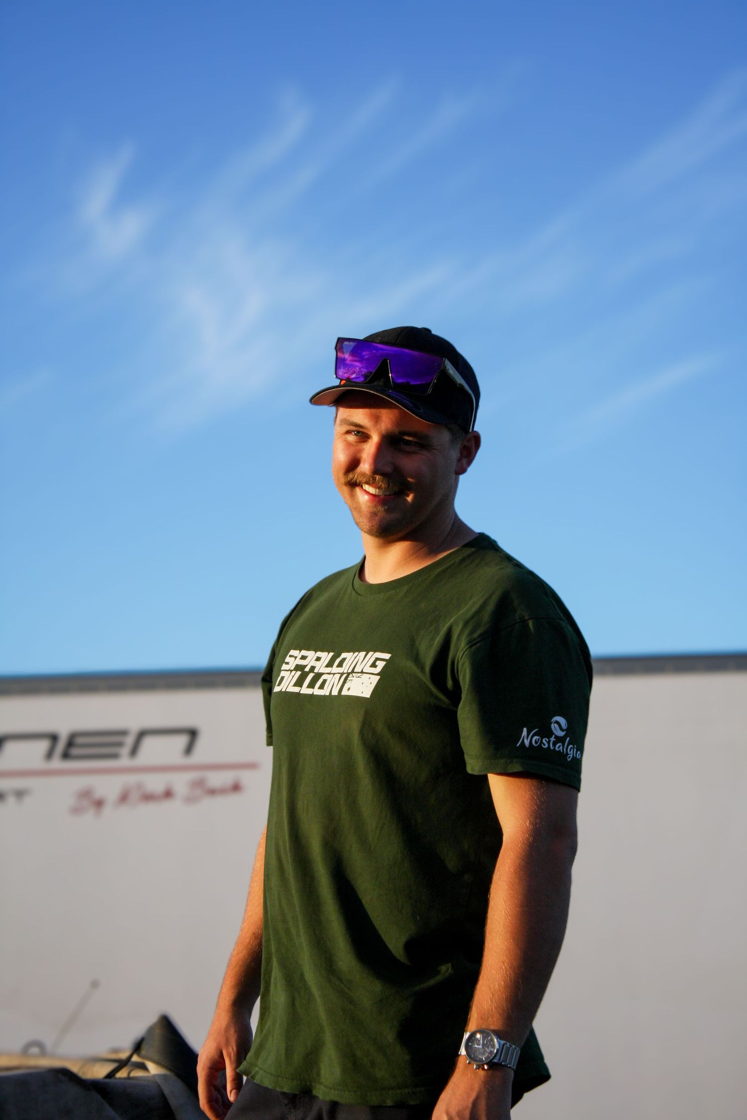 Participant in green shirt and cap stands against blue sky at outdoor event.