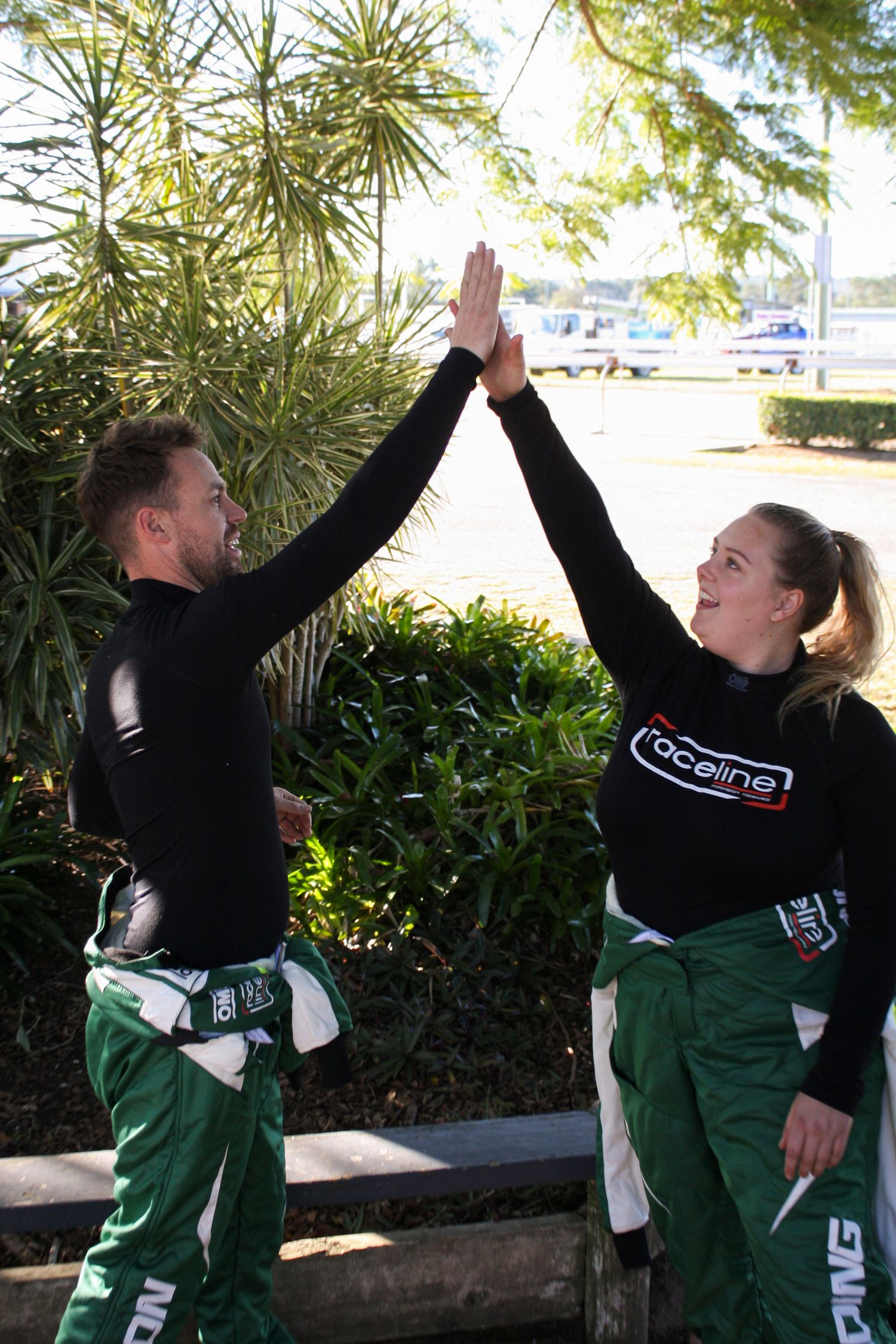 Two team members in racing gear celebrate with a high-five outdoors.